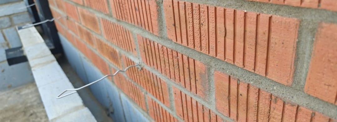 Close-up of red brick wall with wall ties during construction