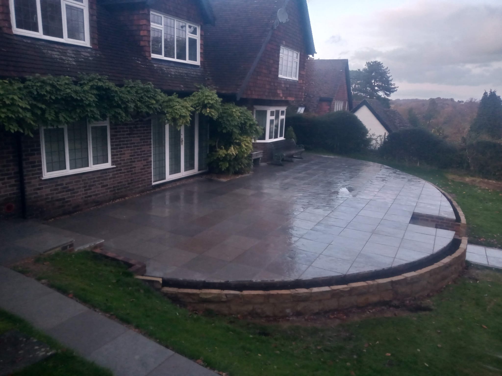 Large curved patio with stone wall and slate paving